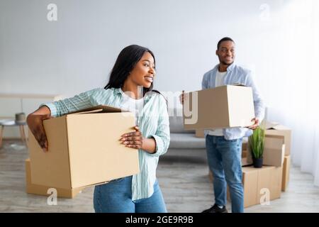 Déménagement et location d'appartement. Un couple noir aimant transportant des boîtes en carton dans une nouvelle maison, marchant dans le salon Banque D'Images