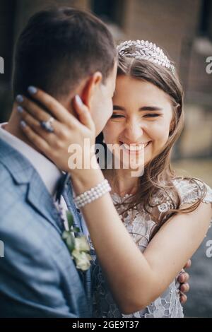 Élégante mariée heureuse et marié souriant et embrassant sur fond de vieille église. Mariage provençal. Beau couple de mariage émotionnel riant et câlin Banque D'Images