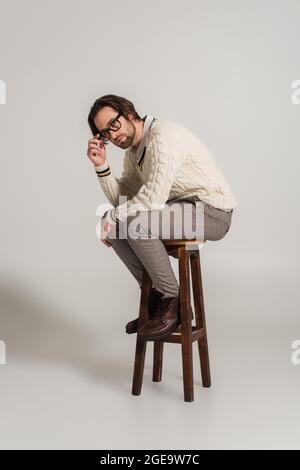 homme en pull blanc et pantalon réglable de lunettes tout en étant assis sur fond gris Banque D'Images