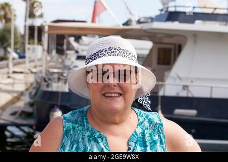 Femme avec pamela et lunettes de soleil pose avec chihuahua dans ses bras avec arrière-plan de port avec des bateaux hors de focus, été, voyage de mer, vacances de bateau. Banque D'Images