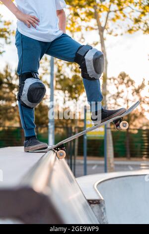 Crop teen skater debout sur le skateboard et se préparant à montrer le truc sur la rampe dans le parc de skate Banque D'Images