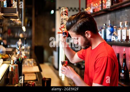 Vue latérale d'un barman concentré qui verse de l'alcool à la bouteille dans un puzzle en métal tout en préparant un cocktail au bar Banque D'Images