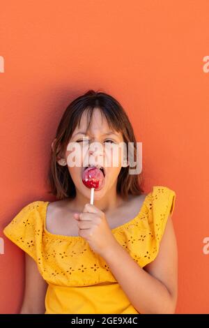 Enfant de couleur jaune avec décoration florale faisant le visage tout en appréciant le bon lally et regardant l'appareil photo Banque D'Images