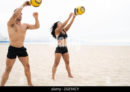 Sport multiracial et sportif effectuant un exercice d'oscillation de kettlebell pendant l'entraînement en bord de mer en été Banque D'Images