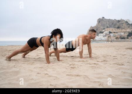 Athlètes multiethniques sportifs, hommes et femmes, qui font des exercices de remise en forme sur un bord de mer sablonneux Banque D'Images