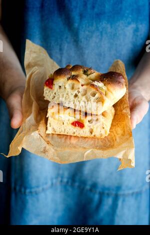 Crop personne mains tenant un morceau de focaccia de tomate fraîche avec le romarin Banque D'Images
