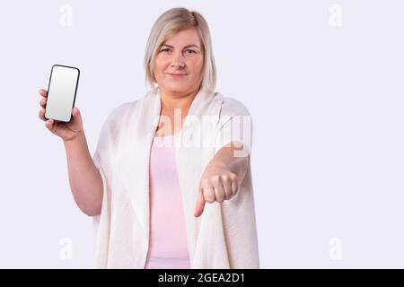 Une femme souriante a coupé des cheveux blonds dans un gilet blanc long tenant un téléphone portable et a atteint un poing. Banque D'Images