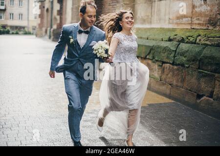 Beau couple de mariage émotif souriant et s'amusant sous la pluie dans la ville européenne. Mariage provençal. Mariée et marié stylés et heureux, courir sur le dos Banque D'Images
