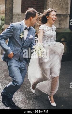 Élégante mariée heureuse et marié courant sur fond de vieille église dans la rue des pluies. Mariage provençal. Beau couple de mariage émotionnel souriant et ha Banque D'Images