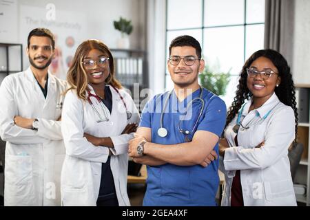 Portrait d'une équipe médicale multiethnique souriante debout dans une salle de clinique moderne avec les bras croisés. Groupe de médecins multiraciaux qualifiés et confiants, qui se posent à l'intérieur avec les bras pliés Banque D'Images