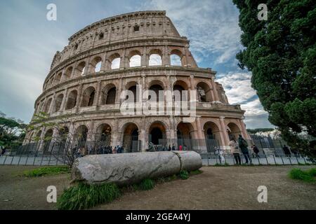 Une colonne déchue se trouve sous l'imposant Colisée tandis que les touristes regardent vers le haut à Rome. Banque D'Images