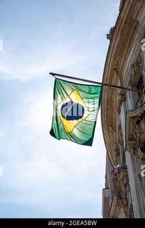 Drapeau brésilien s'affichant sur un poteau devant la maison contre le ciel bleu. Drapeau national du Brésil agitant sur une maison suspendue d'un poteau sur une fron Banque D'Images