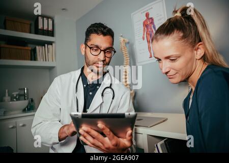 une infirmière féminine de race mixte assise avec un médecin de sexe masculin à l'aide d'une tablette numérique Banque D'Images