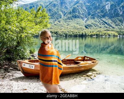 Femme blonde se tenant dans le lac de Bohinj, à côté d'un bateau sur la plage Banque D'Images