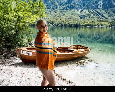 Femme blonde se tenant dans le lac de Bohinj, à côté d'un bateau sur la plage Banque D'Images