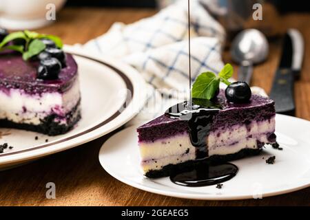 Verser le chocolat sur un délicieux cheesecake maison aux myrtilles garni de myrtilles conservées et de menthe dans un plat en céramique blanche avec l'OMS Banque D'Images