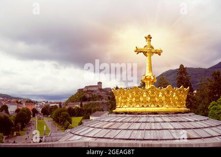 Couronne d'or et croix sur le toit de la Basilique de la Vierge Marie à Lourdes. Le château médiéval en arrière-plan. Banque D'Images