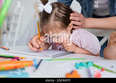 enseignant aidant une fille handicapée avec le syndrome de down dessin près de l'enfant flou dans la maternelle privée Banque D'Images