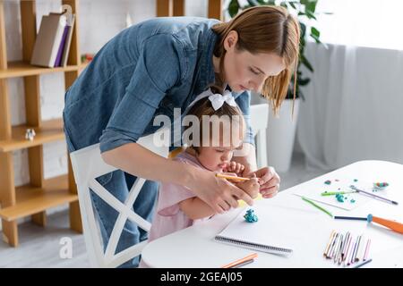 enseignant aidant l'enfant handicapé avec le syndrome de down moulage de la plaline dans la maternelle privée Banque D'Images