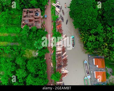 Vue aérienne des constructeurs de bateaux fabriquent des bateaux en bois à "Noukar Haat" (marché de bateaux) à Kuriana sous le Swarupkathi upazila du district de Pirojpur. Le marché de Noukar Haat, d'une longueur de deux kilomètres, est réputé pour le commerce de différentes variétés de bateaux pendant la saison de la mousson. Le marché se déroule tous les vendredis de mai à novembre. “Panis” ou “Pinis”, “Dingi” et “Naak Golui” sont les types de bateaux disponibles à la vente, construits par des artisans locaux des Muktahar, Chami, Boldia, Inderhaat, Boitha Kata, Villages de Dubi et Kathali. Le 18 août 2021 à Barishal, au Bangladesh. Photo de M Banque D'Images