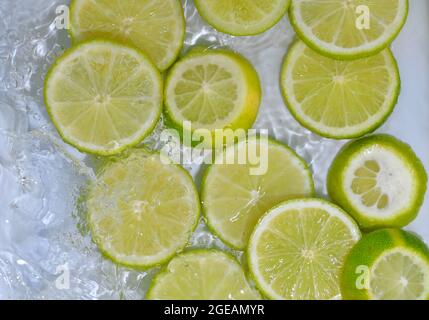 Gros plan sur des tranches fraîches de limes vertes sur fond blanc. Tranches de limes dans l'eau pétillante sur fond blanc, gros plan. Citron soda Banque D'Images