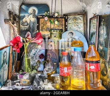 L'intérieur d'un sanctuaire grec orthodoxe en bord de route présentant des icônes religieuses, des bouteilles d'huile sainte et des brûleurs à encens. Arcadia, Péloponnèse, Grèce Banque D'Images