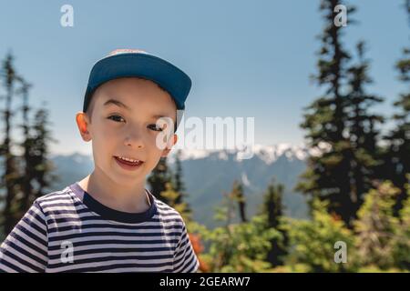 Jeune garçon souriant avec les montagnes olympiques derrière, sur Hurricane Hill dans le parc national olympique. Banque D'Images