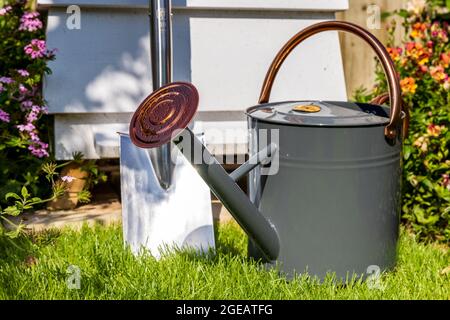 Arrosoir traditionnel en métal et bêche de jardin avec une ruche en arrière-plan Banque D'Images