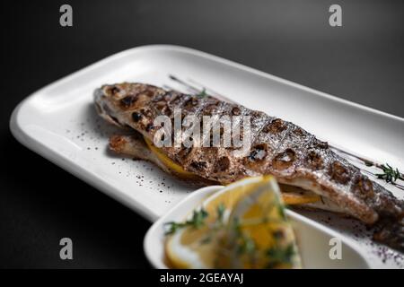 gros plan de poisson farci grillé entier avec citron sur l'assiette sur fond noir Banque D'Images