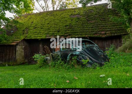 Vieille voiture bleue dans de l'herbe verte longue près de l'ancienne grange brune en bois Banque D'Images