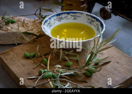 Olives vertes et branche sur une planche en bois avec un bol et une bouteille d'huile d'olive pressée à froid. Banque D'Images