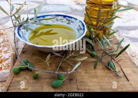 Olives vertes et branche sur une planche en bois avec un bol et une bouteille d'huile d'olive pressée à froid. Banque D'Images