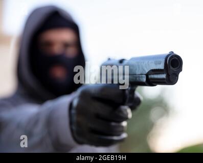 Tueur à capuche avec balaclava, tenant un pistolet dans la main gantée, arme de robber concept. Homme visant avec un pistolet, la nature à l'extérieur arrière-plan, vue rapprochée. Banque D'Images