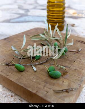 Olives vertes et branche d'olive sur une planche en bois avec une bouteille d'huile d'olive. Banque D'Images