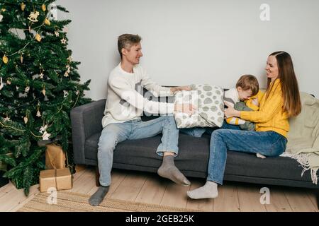 Bonne famille mère, père et garçon combattent des oreillers à la maison dans le canapé. Arbre de Noël. Banque D'Images