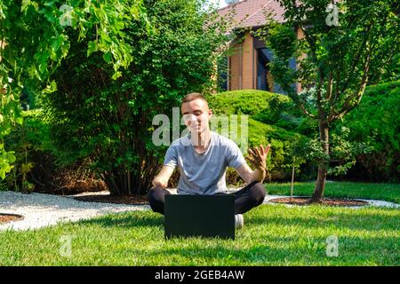 Un gars avec un bras amputé s'assoit sur la pelouse et parle avec des amis via le réseau social Banque D'Images