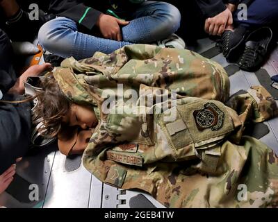 Un enfant afghan dort sur le plancher de cargaison d'une US Air Force C-17 Globemaster III, maintenue au chaud par l'uniforme de la première classe d'Airman Nicolas Baron, chardmaster C-17, lors d'un vol d'évacuation en provenance de Kaboul, Afghanistan, le 18 août 2021. L'exploitation d'une flotte de la Garde nationale aérienne, de la Réserve de la Force aérienne et du Commandement de la mobilité aérienne, en appui au ministère de la Défense, a amené des forces sur le théâtre afin de faciliter le départ et le déplacement en toute sécurité des citoyens américains, des bénéficiaires de visas d'immigration spéciaux et des populations afghanes vulnérables en provenance d'Afghanistan. (Photo : 1er lieutenant Mark Lawson) Banque D'Images