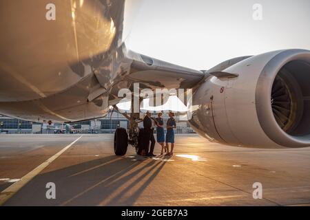 Avion près du terminal dans un aéroport au coucher du soleil. Pilote et deux hôtesses debout et parlant après l'atterrissage ou avant le départ Banque D'Images