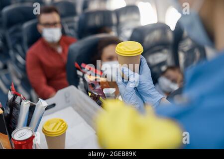 Gros plan des mains dans les gants de protection du préposé aux vols servant des boissons aux passagers à bord. Voyager en avion pendant la pandémie de Covid19 Banque D'Images