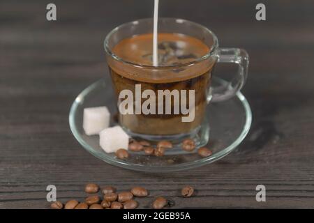 Une tasse en verre et une soucoupe placées sur un fond en bois sombre. Il est rempli d'un liquide brun, c'est du café filtre. Il y a des cubes de sucre et du café bea Banque D'Images