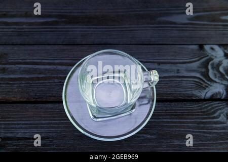 Une tasse en verre avec une soucoupe placée sur un substrat en bois noir fait de planches. Banque D'Images