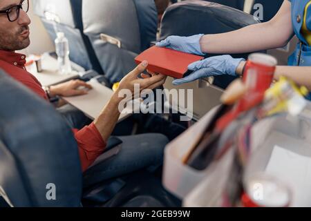 Gros plan des mains d'un passager de sexe masculin qui reçoit une boîte à lunch de la part d'un préposé de vol de sexe féminin servant de la nourriture à bord Banque D'Images