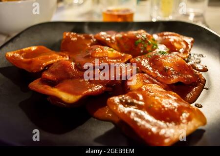 Raviolis italiens traditionnels fourrés de ricotta, servis avec une sauce tomate et des feuilles de basilic sur une assiette noire Banque D'Images