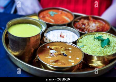 Une plaque en acier de sens thali indien contenant différents aliments sur un plateau rond comme le riz Basmati, le caillé ou le raita, le poulet au beurre et le mangue Banque D'Images