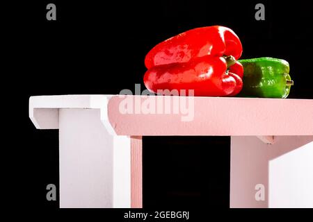 Photographie d'un poivron rouge et d'un poivron vert italien sur un banc blanc et un fond noir. La photo est prise en format horizontal et a un espace de copie Banque D'Images