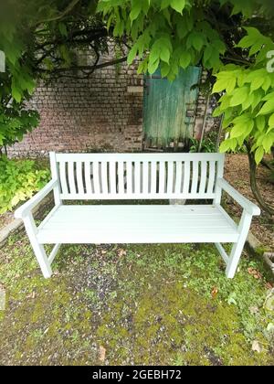 Siège de jardin en premier plan avec feuillage au-dessus et porte de jardin dans le mur derrière. Photo de haute qualité avec espace de copie. Banque D'Images