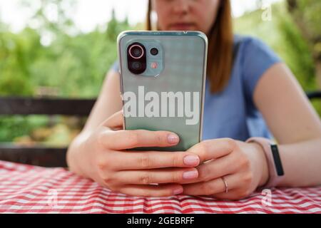 Téléphone portable entre les mains d'une femme caucasienne inconnue, assis à la table en été Banque D'Images