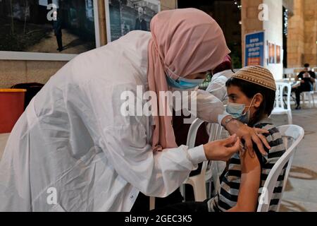 Un agent de santé arabe israélien administre une dose du vaccin Pfizer-BioNtech COVID-19 à un jeune juif religieux au centre de vaccination nocturne du complexe de la mairie le 17 août 2021 à Jérusalem, en Israël. Israël a encouragé la vaccination de plus de jeunes, citant de nouvelles épidémies attribuées à la variante plus infectieuse du delta. Banque D'Images