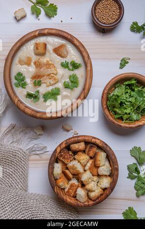 Plat avec soupe à la crème de chou-fleur blanc fraîchement faite, herbes vertes fraîches et croûtons dans des bols en bois sur table blanche en bois. Serviette en lin, moutarde s Banque D'Images