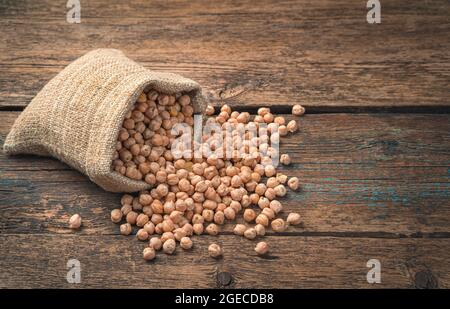 Séchez les pois chiches dans un sac de lin sur un fond marron en bois. Vue latérale. Une alimentation saine. Banque D'Images